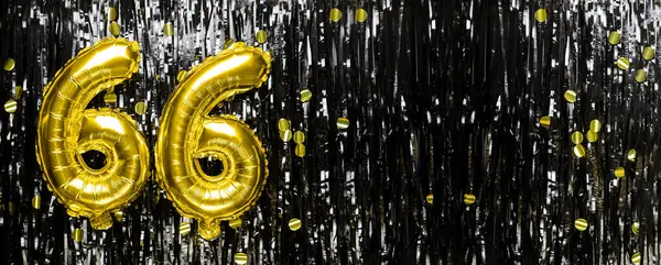 Gold foil balloon number number 66 on a background of black tinsel decoration. Birthday greeting card, inscription sixty-six. Anniversary event. Banner. copy space.