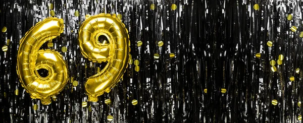 Gold foil balloon number number 69 on a background of black tinsel decoration. Birthday greeting card, inscription sixty-nine. Anniversary event. Banner. copy space.