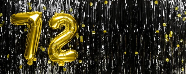 Gold foil balloon number number 72 on a background of black tinsel decoration. Birthday greeting card, inscription seventy-two. Anniversary event. Banner. copy space.