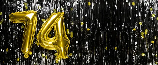 Gold foil balloon number number 74 on a background of black tinsel decoration. Birthday greeting card, inscription seventy-four. Anniversary event. Banner. copy space.