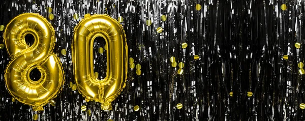 Gold foil balloon number number 80 on a background of black tinsel decoration. Birthday greeting card, inscription eighty. Anniversary event. Banner. copy space.