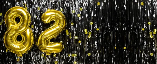 Gold foil balloon number number 82 on a background of black tinsel decoration. Birthday greeting card, inscription eighty-two. Anniversary event. Banner. copy space.