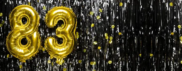 Gold foil balloon number number 83 on a background of black tinsel decoration. Birthday greeting card, inscription eighty-three. Anniversary event. Banner. copy space.