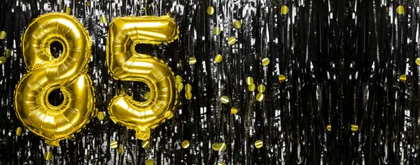 Gold foil balloon number number 85 on a background of black tinsel decoration. Birthday greeting card, inscription eighty-five. Anniversary event. Banner. copy space.