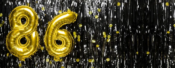 Gold foil balloon number number 86 on a background of black tinsel decoration. Birthday greeting card, inscription eighty-six. Anniversary event. Banner. copy space.
