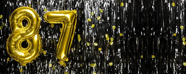 Gold foil balloon number number 87 on a background of black tinsel decoration. Birthday greeting card, inscription eighty-seven. Anniversary event. Banner. copy space.