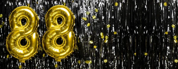 Gold foil balloon number number 88 on a background of black tinsel decoration. Birthday greeting card, inscription eighty-eight. Anniversary event. Banner. copy space.