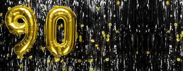 Gold foil balloon number number 90 on a background of black tinsel decoration. Birthday greeting card, inscription ninety. Anniversary event. Banner. copy space.