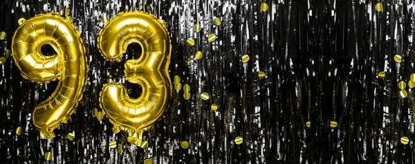 Gold foil balloon number number 93 on a background of black tinsel decoration. Birthday greeting card, inscription ninety-three. Anniversary event. Banner. copy space.