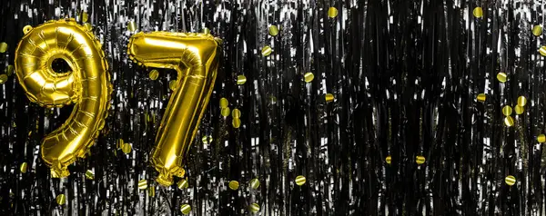 Gold foil balloon number number 97 on a background of black tinsel decoration. Birthday greeting card, inscription ninety-seven. Anniversary event. Banner. copy space.
