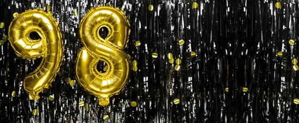 Gold foil balloon number number 98 on a background of black tinsel decoration. Birthday greeting card, inscription ninety-eight. Anniversary event. Banner. copy space.