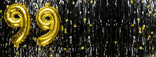 Gold foil balloon number number 99 on a background of black tinsel decoration. Birthday greeting card, inscription ninety-nine. Anniversary event. Banner. copy space.