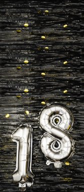 Altın konfetiyle süslenmiş siyah süslemenin arka planında 18 numaralı gümüş folyo balon. Doğum günü tebrik kartı, 18. yazı. Yıldönümü etkinliği. Dikey Sancak. Boşluğu kopyala.