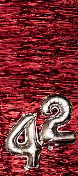 Silver foil balloon number number 42 on a background of red tinsel decoration. Birthday greeting card, inscription forty-two. Anniversary event. Vertical Banner. copy space.
