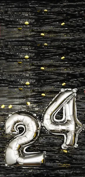 Silver foil balloon number 24 on a background of black tinsel decoration with golden confetti. Birthday greeting card, inscription twenty-four. Anniversary event. Vertical Banner. copy space.