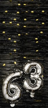 Altın konfetiyle siyah süslemeli arka planda 63 numaralı gümüş folyo balonu. Doğum günü kartı, yazıt altmış üç. Yıldönümü etkinliği. Dikey afiş. Boşluğu kopyala.