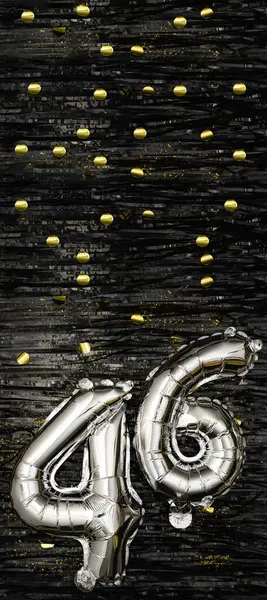 Silver foil balloon number 46 on a background of black tinsel with gold confetti. Birthday card, inscription forty-sixth. Anniversary event. Vertical banner. copy space.