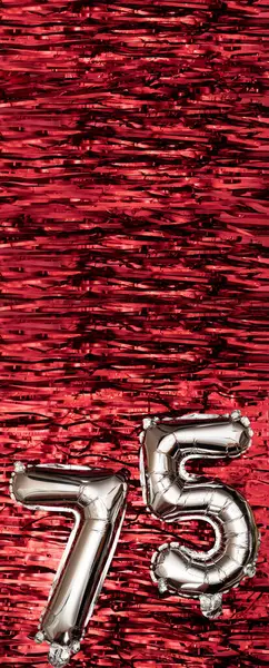 Silver foil balloon number 75 on a background of red tinsel decoration. Birthday greeting card, inscription seventy-five. Anniversary event. Vertical Banner. copy space.
