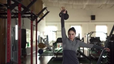 Spor kıyafetli genç, zayıf bir kadın spor salonunda ağırlık çalışırken dambıl kaldırıyor. Boşluğu kopyala
