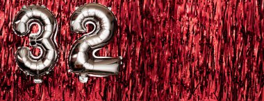 Gümüş folyo balonu 32 numara. 32. yazıyla birlikte doğum günü tebrik kartı. Yıldönümü kutlaması. Pankart. Kırmızı arka planda gümüş rakam. Boşluğu kopyala