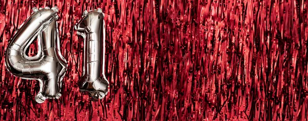 Silver foil balloon number 41 on a background of red tinsel decoration. Birthday greeting card, inscription forty-one. Anniversary event. Banner. copy space.
