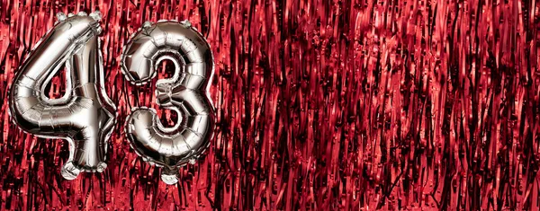 Silver foil balloon number 43 on a background of red tinsel decoration. Birthday greeting card, inscription forty-three. Anniversary event. Banner. copy space.