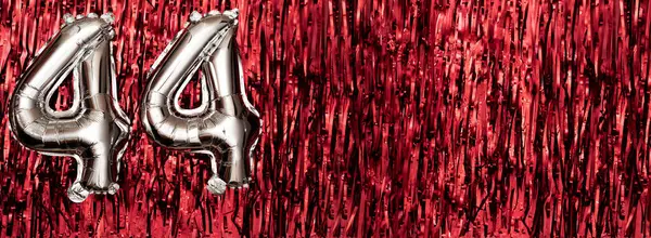 Silver foil balloon number 44 on a background of red tinsel decoration. Birthday greeting card, inscription forty-four. Anniversary event. Banner. copy space.