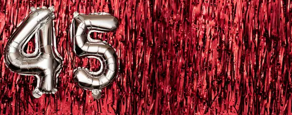 Silver foil balloon number 45 on a background of red tinsel decoration. Birthday greeting card, inscription forty-five. Anniversary event. Banner. copy space.