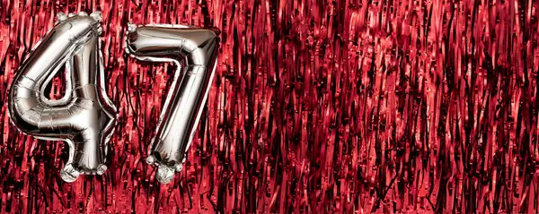 Silver foil balloon number 47 on a background of red tinsel decoration. Birthday greeting card, inscription forty-seven. Anniversary event. Banner. copy space.