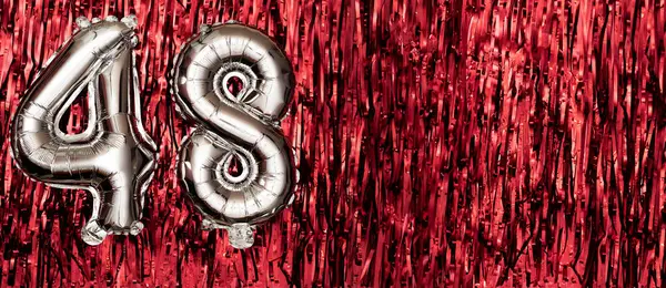 Silver foil balloon number 48 on a background of red tinsel decoration. Birthday greeting card, inscription forty-eight. Anniversary event. Banner. copy space.