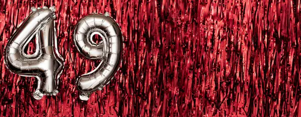 Silver foil balloon number 49 on a background of red tinsel decoration. Birthday greeting card, inscription forty-nine. Anniversary event. Banner. copy space.