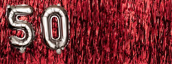 Silver foil balloon number 50 on a background of red tinsel decoration. Birthday greeting card, inscription fifty. Anniversary event. Banner. copy space.