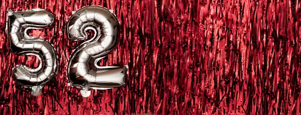 Silver foil balloon number fifty-two. Birthday or anniversary card with the inscription 52. Red tinsel background. Anniversary celebration. Banner. copy space