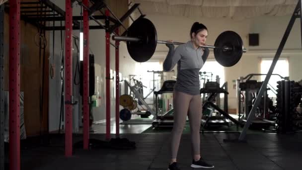 女运动员在体育馆里用一个沉重的杠铃蹲着 女健美运动员做硬核训练设施 复制空间 — 图库视频影像