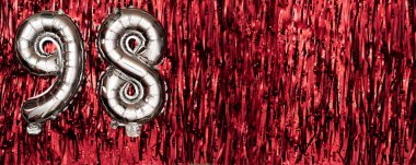 Gümüş folyo balonu 99 numara. Doğum günü ya da yıldönümü kartında 99 yazılıydı. Kırmızı süslemeli arka plan. Yıldönümü kutlaması. Pankart. Boşluğu kopyala