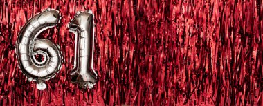 Gümüş folyo balon numarası, kırmızı arka planda 61 numara. Doğum günü tebrik kartında 61 yazılıydı. Yıldönümü kutlaması. Pankart. Sayısal rakam