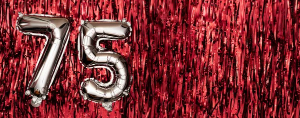 Silver foil balloon number seventy-five. Birthday or anniversary card with the inscription 75. Red tinsel background. Anniversary celebration. Banner. copy space