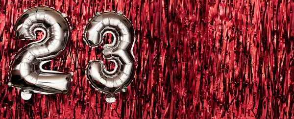 Silver foil balloon number twenty-three. Birthday greeting card with inscription 23. Anniversary celebration. Banner. Silver numeral on red background. Copy space