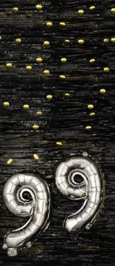 Gümüş folyo balonu 99 numara. Doğum günü ya da yıldönümü kartı 99 yazılıydı. Siyah süslemeli arka plan. Yıldönümü kutlaması. Dikey Sancak. Boşluğu kopyala