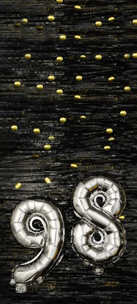 Silver foil balloon number ninety-eight. Birthday or anniversary card with the inscription 98. Black tinsel background. Anniversary celebration. Vertical Banner. copy space