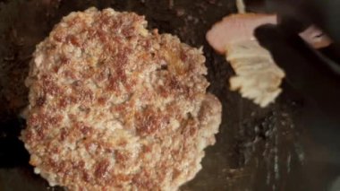 Amerikan hamburgeri pişiriyorum. Sığır pirzolası ve pastırma dilimleri, yakın plan. Mutfakta aşçı fast food restoranında hamburgerler için pirzola yapıyor. Dikey video