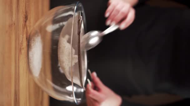 ガラスボウルでふるいによって小麦粉をふるう女性の手のゆっくりとした動きのショット バーティカルビデオ — ストック動画