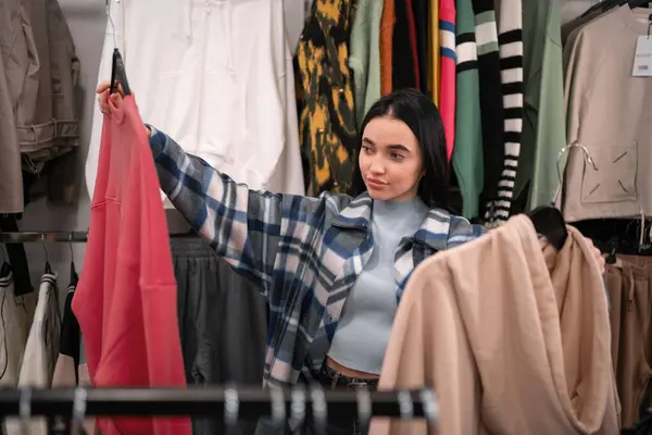 Casual young woman chooses spring clothes in a clothing store. Copy space
