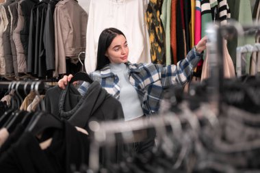 Giyim mağazasından kıyafet seçen genç ve güzel bir bayan alıcı. Satış sırasında moda mağazasından kıyafet alıyor. Boşluğu kopyala