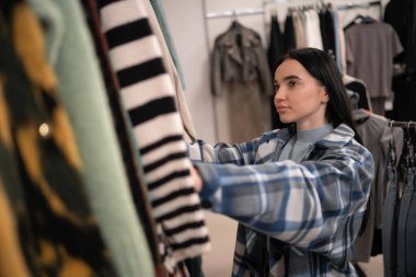 Alışveriş konsepti. Genç esmer bayan moda mağazasında moda kıyafetlerini seçiyor. Boşluğu kopyala