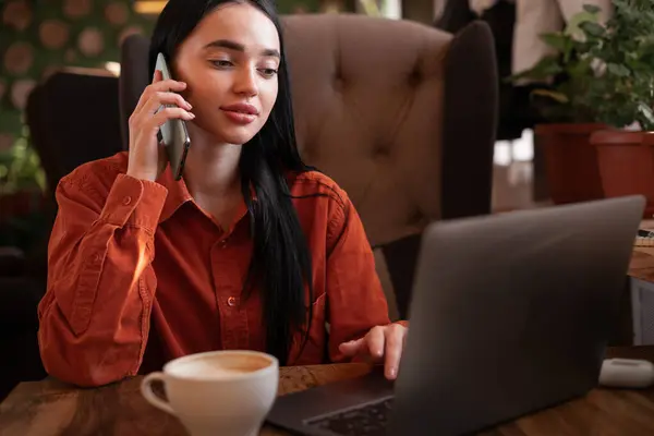 Serious young web store owner calling to client to confirm ordering of purchase, content managers monitoring work of site while sitting in cafe uses laptop computer. Copy space
