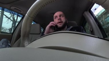 Sakallı adam araba kullanırken telefonda konuşuyor. Araba sürerken sohbet etmek. Direksiyonun başında dikkati dağılmış bir sürücü, düşük açı. Boşluğu kopyala