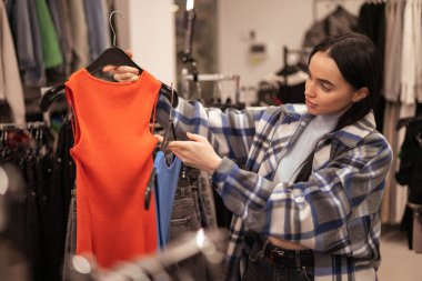 Alışveriş merkezinde ya da giyim mağazasında kıyafet seçen mutlu genç bir kadın aynanın önünde giyinmeyi deniyor. Satış, moda, tüketim ve insan konsepti. Boşluğu kopyala