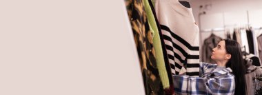 Satış, alışveriş, moda ve insan konsepti. Ceketli genç bir kadın alışveriş merkezinde ya da giyim mağazasında süveter seçiyor. Pankart. Boşluğu kopyala