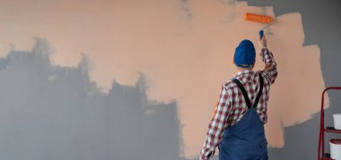 Duvarı turuncu renge boyayan ressamın arka görüntüsü, boya silindiriyle, büyük boş alana. Pankart. Boşluğu kopyala